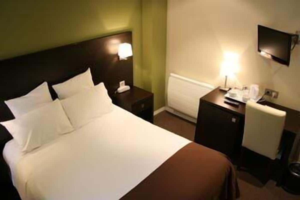 A hotel room with a bed, bedside tables, a lamp, and a flat-screen TV.
