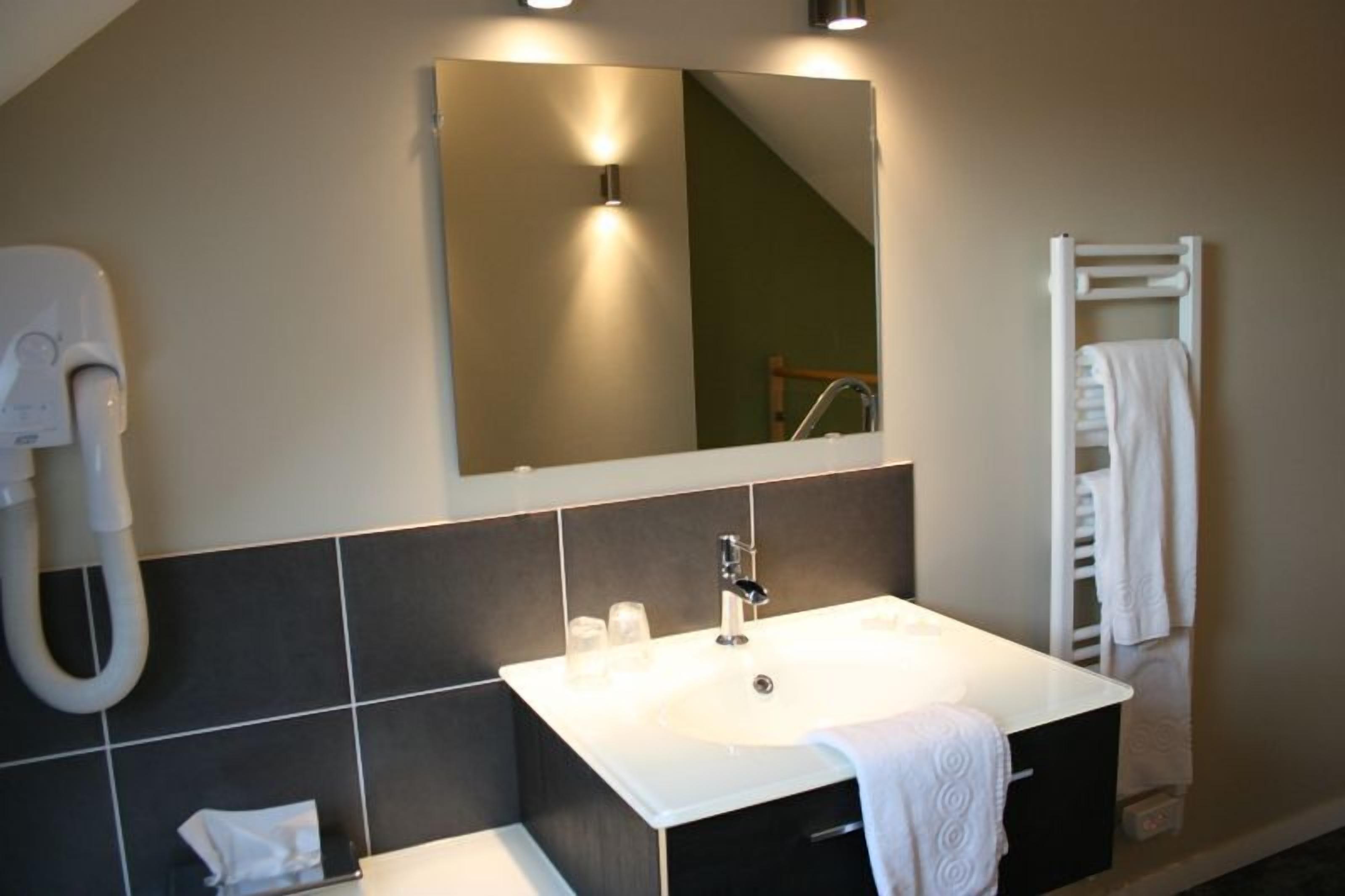 A modern bathroom with a white sink, dark tiles, a large mirror, and a towel rack.