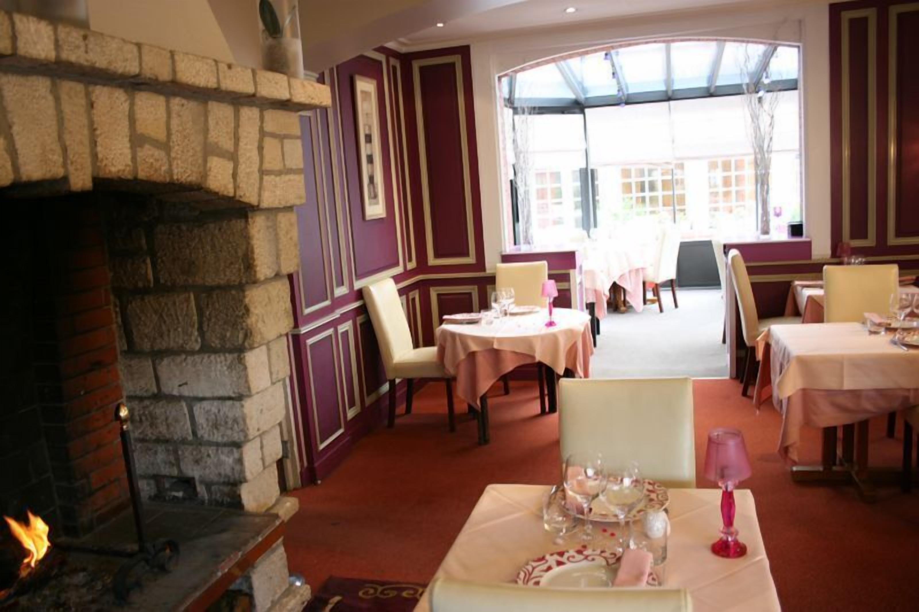 A restaurant with a stone fireplace, tables set for dining, and a view through large windows.