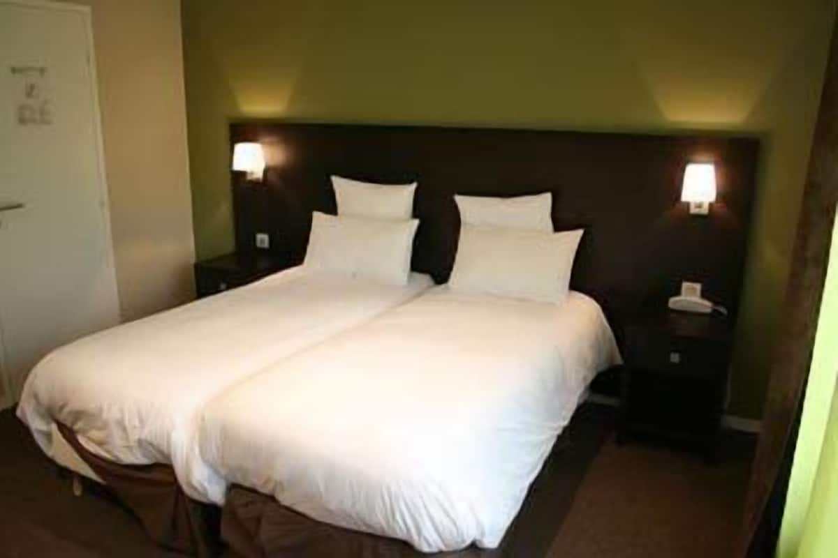 A double bed with white linens in a hotel room.