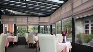 Un comedor interior con mesas y sillas, ventanas amplias y un techo de cristal.