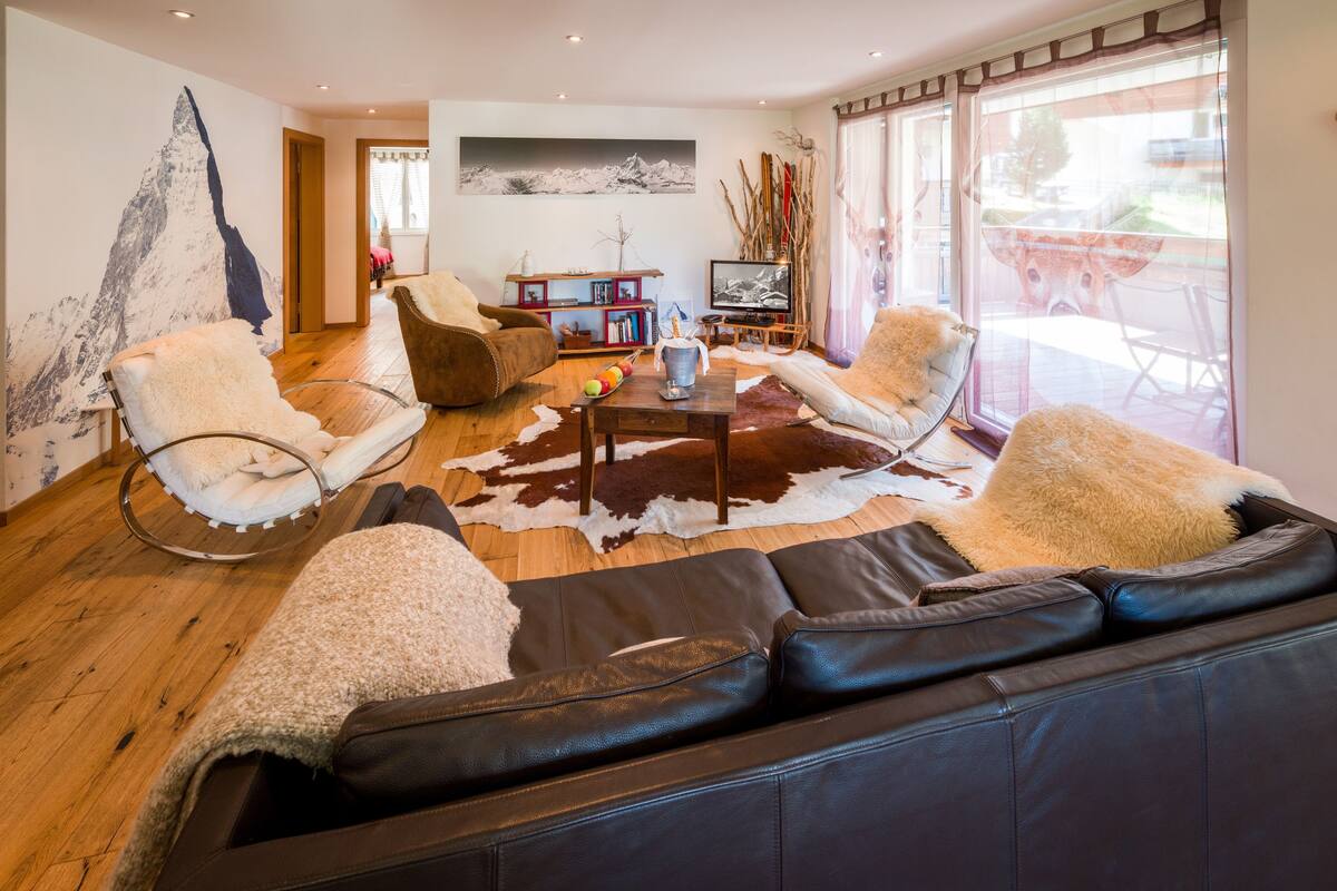 A modern living room with leather sofas, a wooden coffee table, and a large window with a view.