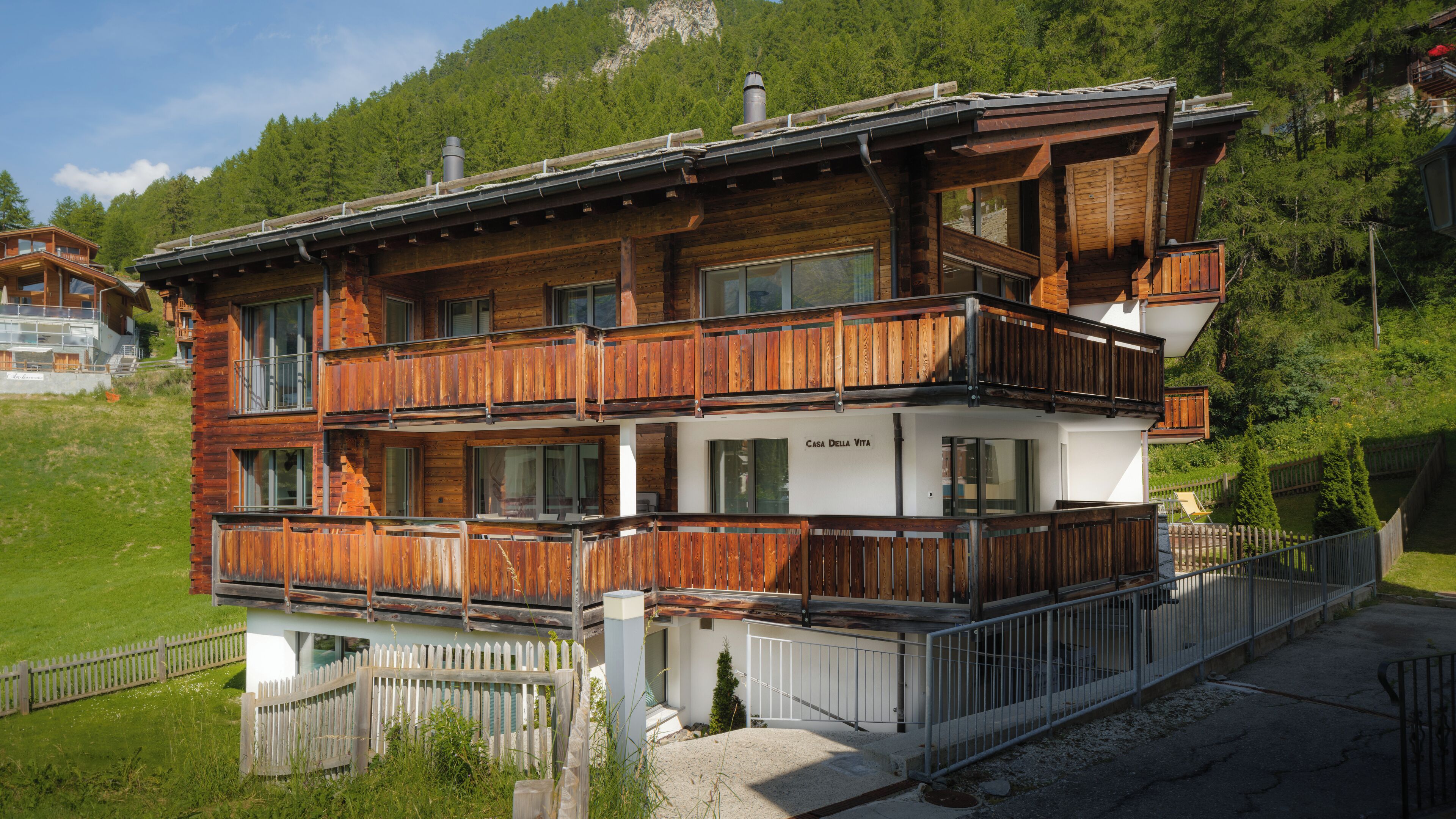 Eine mehrstöckige Holzhütte mit Balkonen, einer weißen Fassade und einem Berg im Hintergrund.