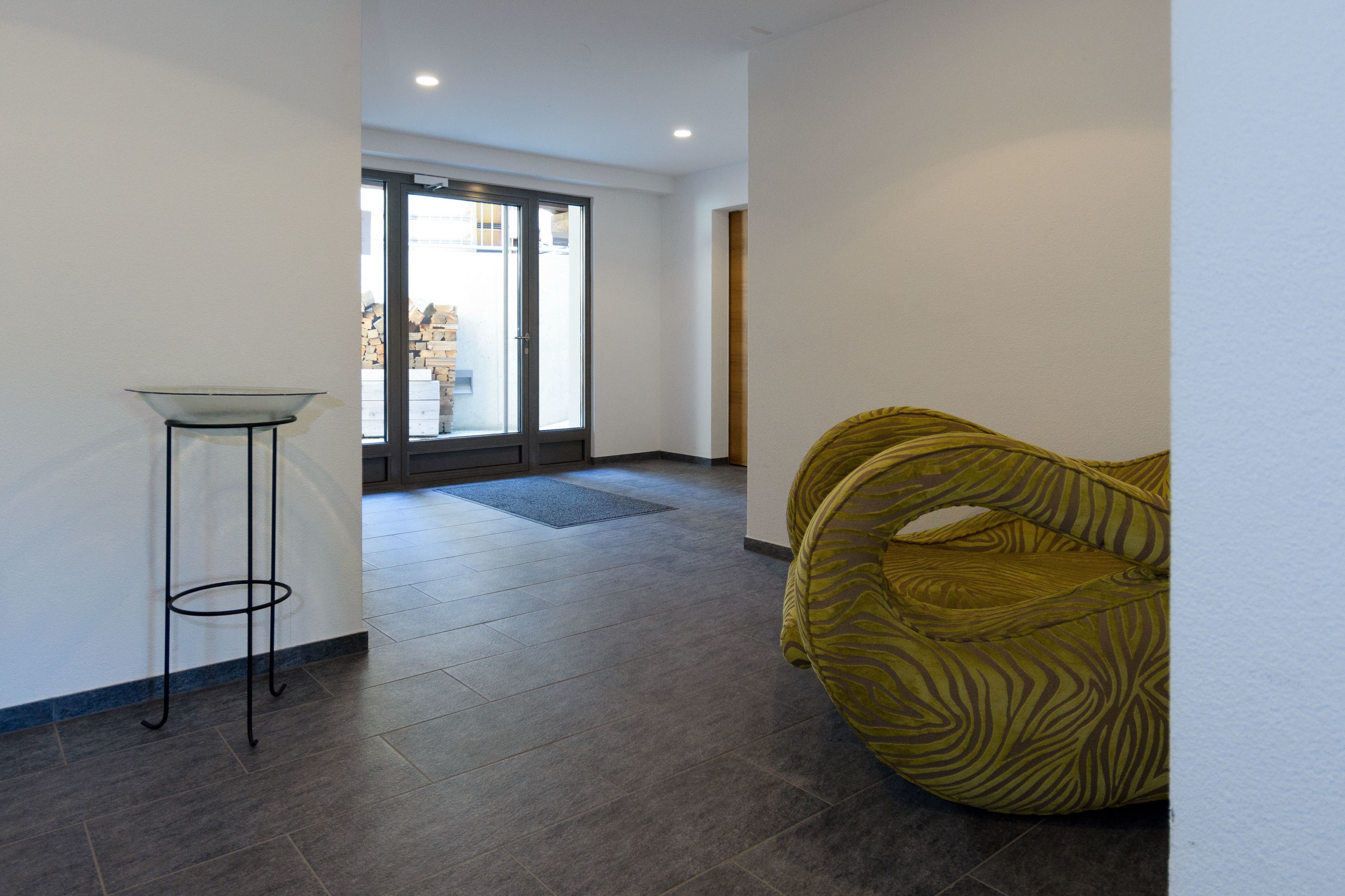 Un couloir avec une porte vitrée donnant sur un espace extérieur, une petite table et une chaise à motifs zébrés.