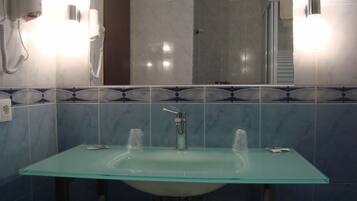 A bathroom with a glass sink, two mirrors, a hairdryer, and a towel rack.