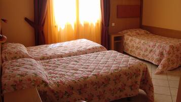 Une chambre d’hôtel avec deux lits, chacun recouvert d’une literie à motifs floraux. On y trouve une tête de lit en bois, une petite table et une chaise.