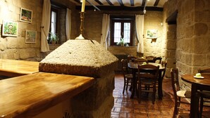 Un interior rústico con paredes de piedra, mobiliario de madera y una hogaza de pan como elemento central.