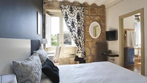 Un dormitorio con cama, televisor, espejo y ventana con cortinas.