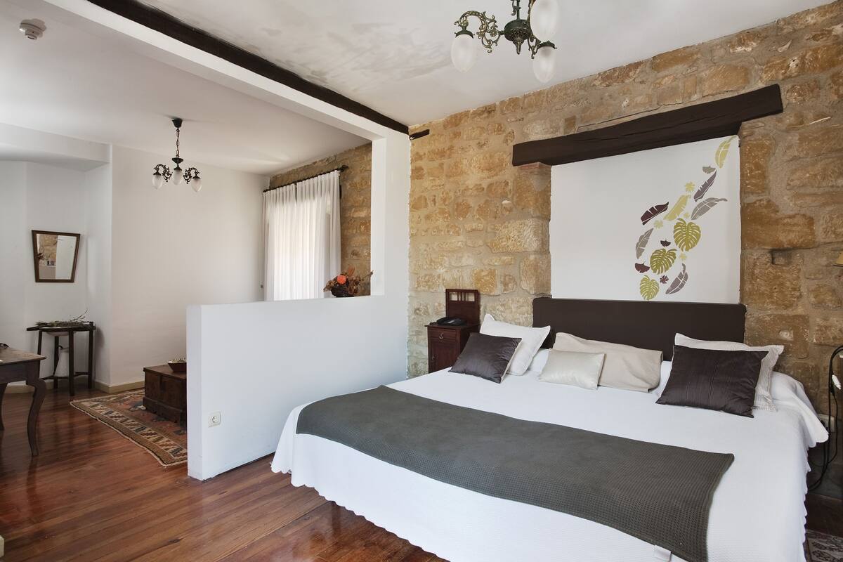 Un dormitorio con una cama grande, una pared de piedra, una araña y vistas al exterior.