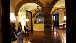 Una habitación con un piano, una silla y una mesa con una lámpara. Se observan dos arcos en el espacio.