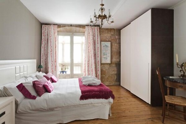 A bedroom with a bed, a wooden floor, a chandelier, a window with curtains, and a desk with a chair. - Rusticae Hospedería Señorío de Briñas (Brinas)