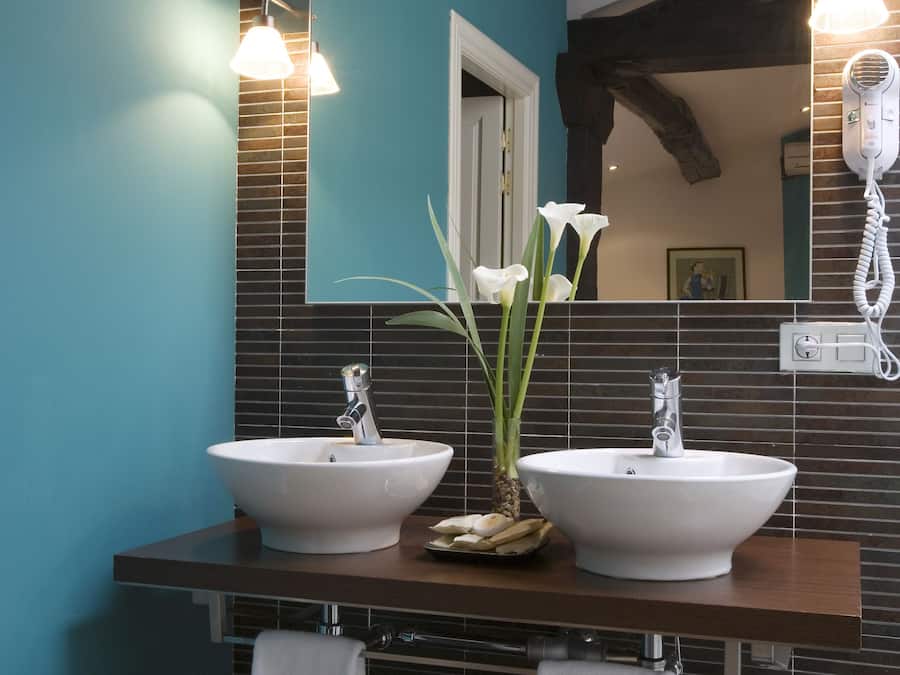 Un baño con dos lavamanos blancos, un espejo y un secador de pelo.