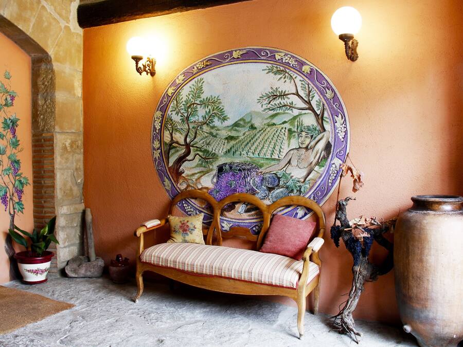 Una habitación acogedora con un banco de madera, un jarrón grande y un muro decorativo con un mural.