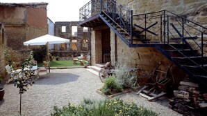Un patio con un edificio de piedra, mobiliario exterior, una escalera y una carretilla.