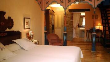 A hotel room with a bed, a chair, a desk, and a bathroom visible through an archway.
