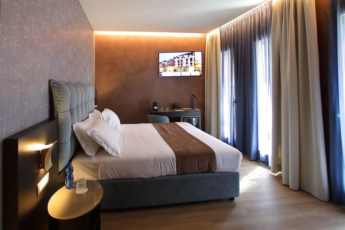Een moderne hotelkamer met een groot bed, een nachtkastje met een lamp, een flatscreen televisie aan de muur en een raam met gordijnen.