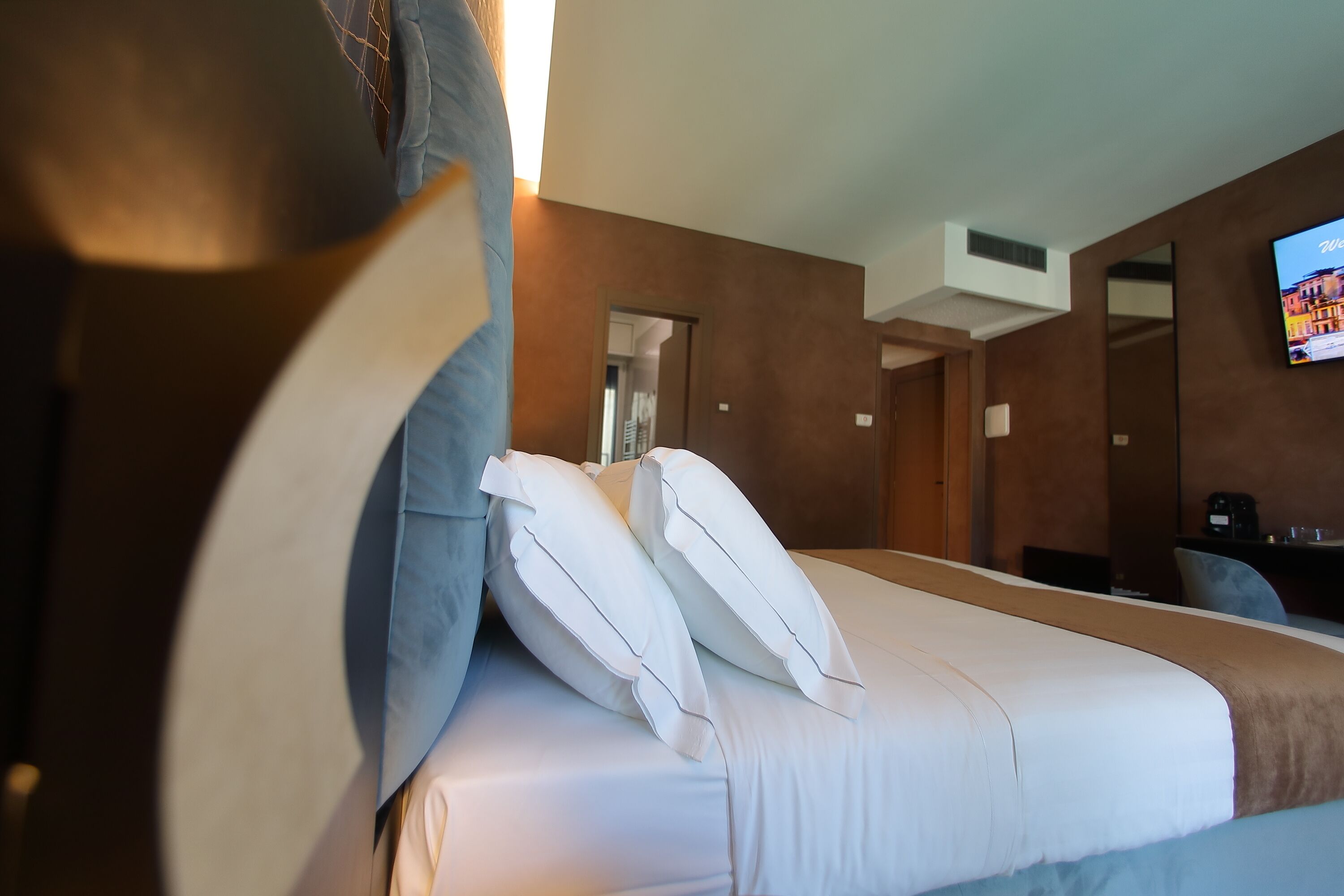 A hotel room with a bed, pillows, a TV, and a desk with a chair.