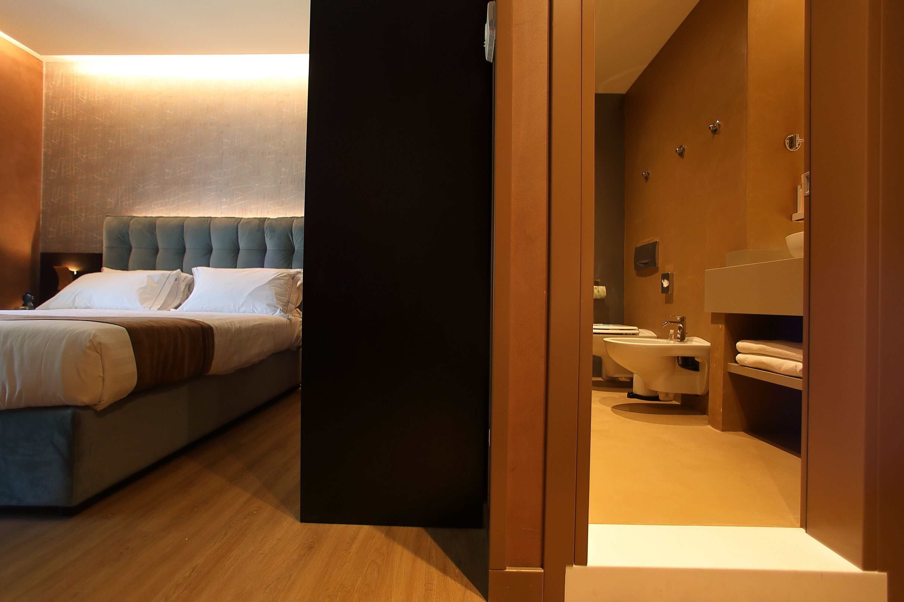A modern hotel room with a large bed, a bedside table, and a bathroom with a sink and toilet.