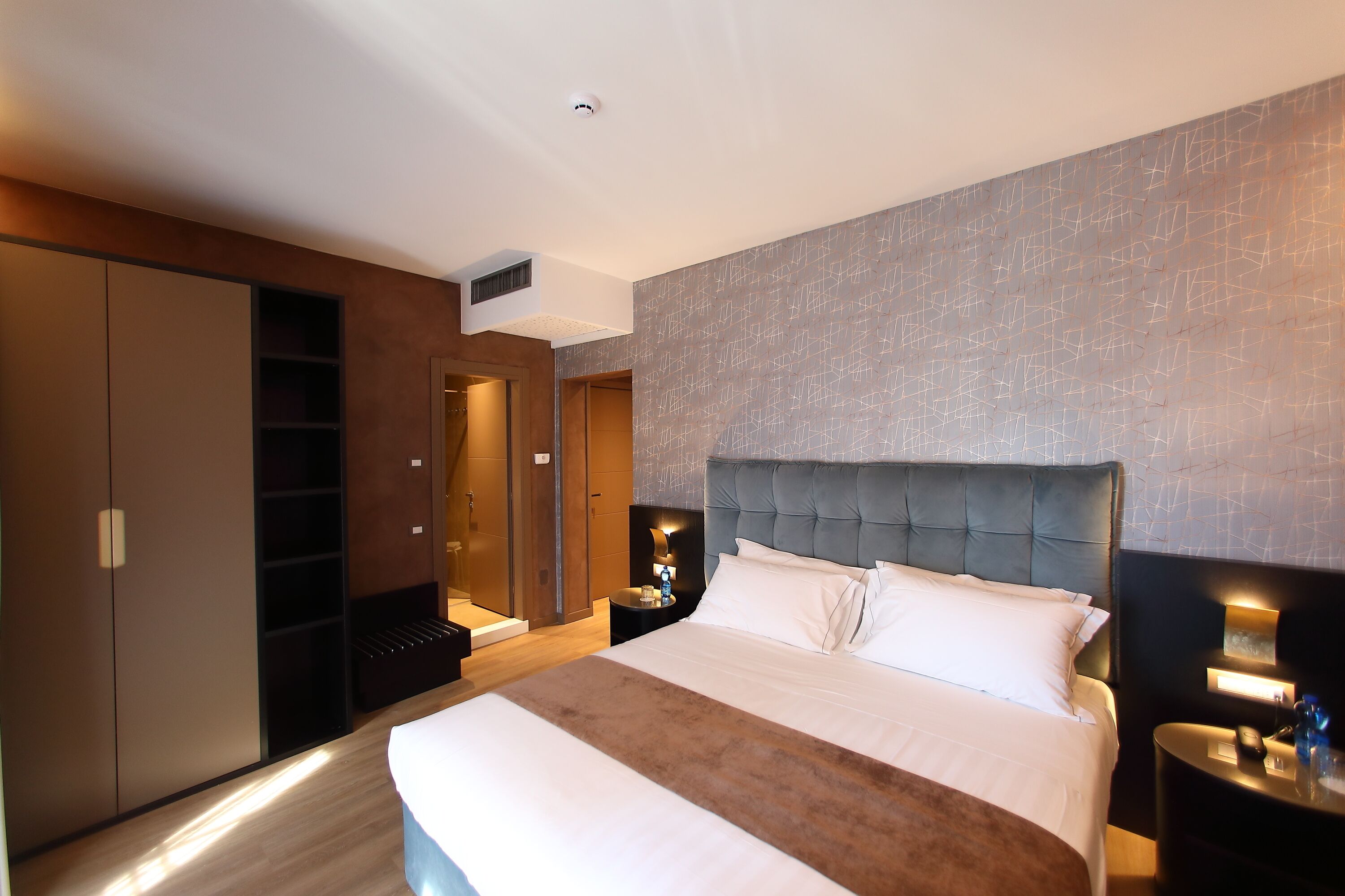 A modern hotel room with a large bed, a wardrobe, a bedside table, and a nightstand.