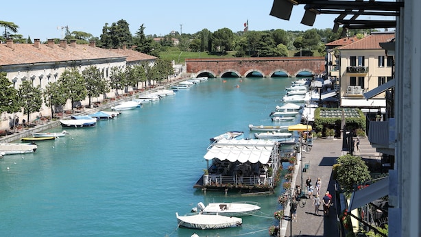 Un canal bordé de bateaux amarrés, un pont en arrière-plan et des bâtiments dotés de balcons donnant sur l’eau.