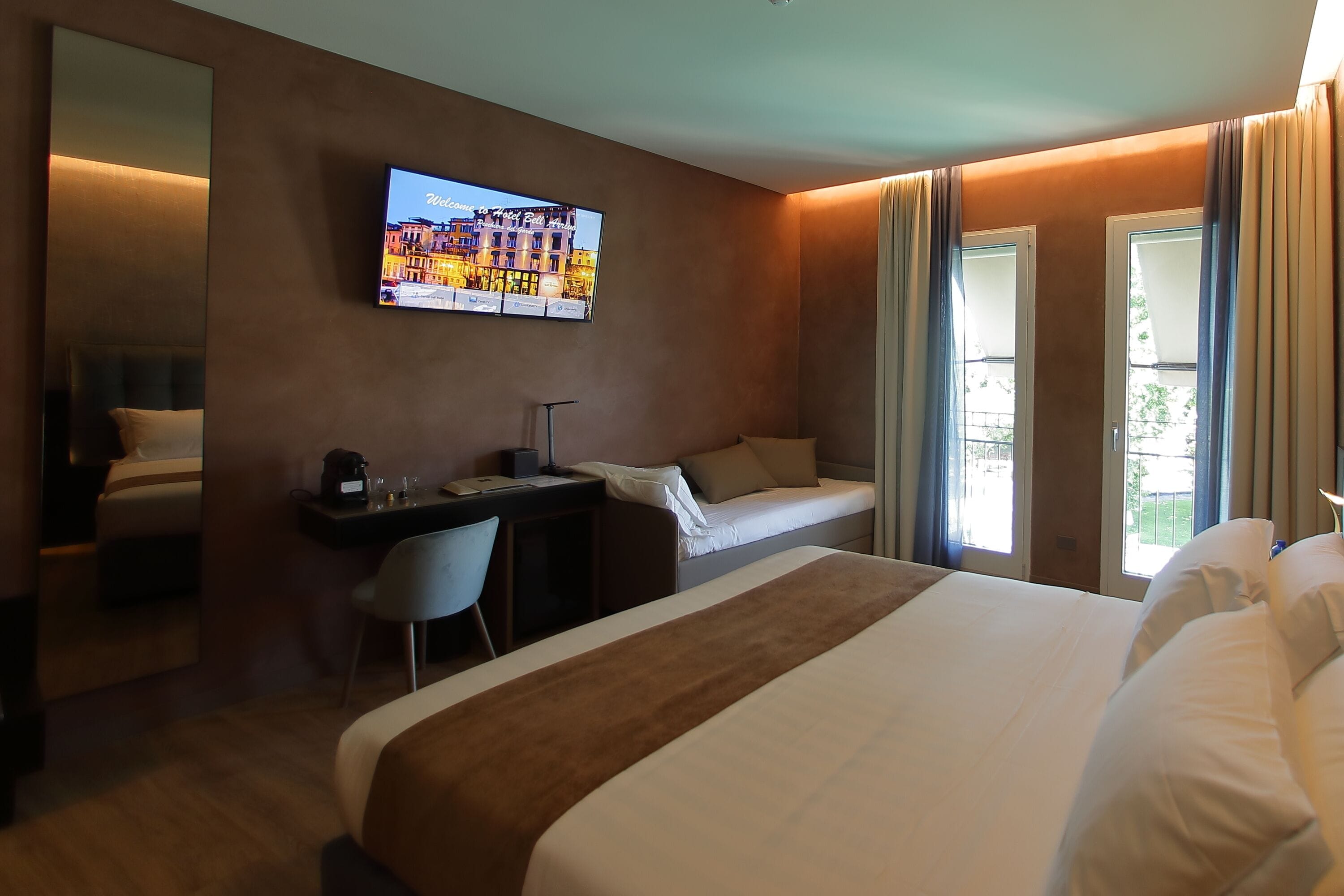 Ett hotellrum med en stor säng, ett skrivbord med en stol, en tv som är monterad på väggen och ett fönster med gardiner.