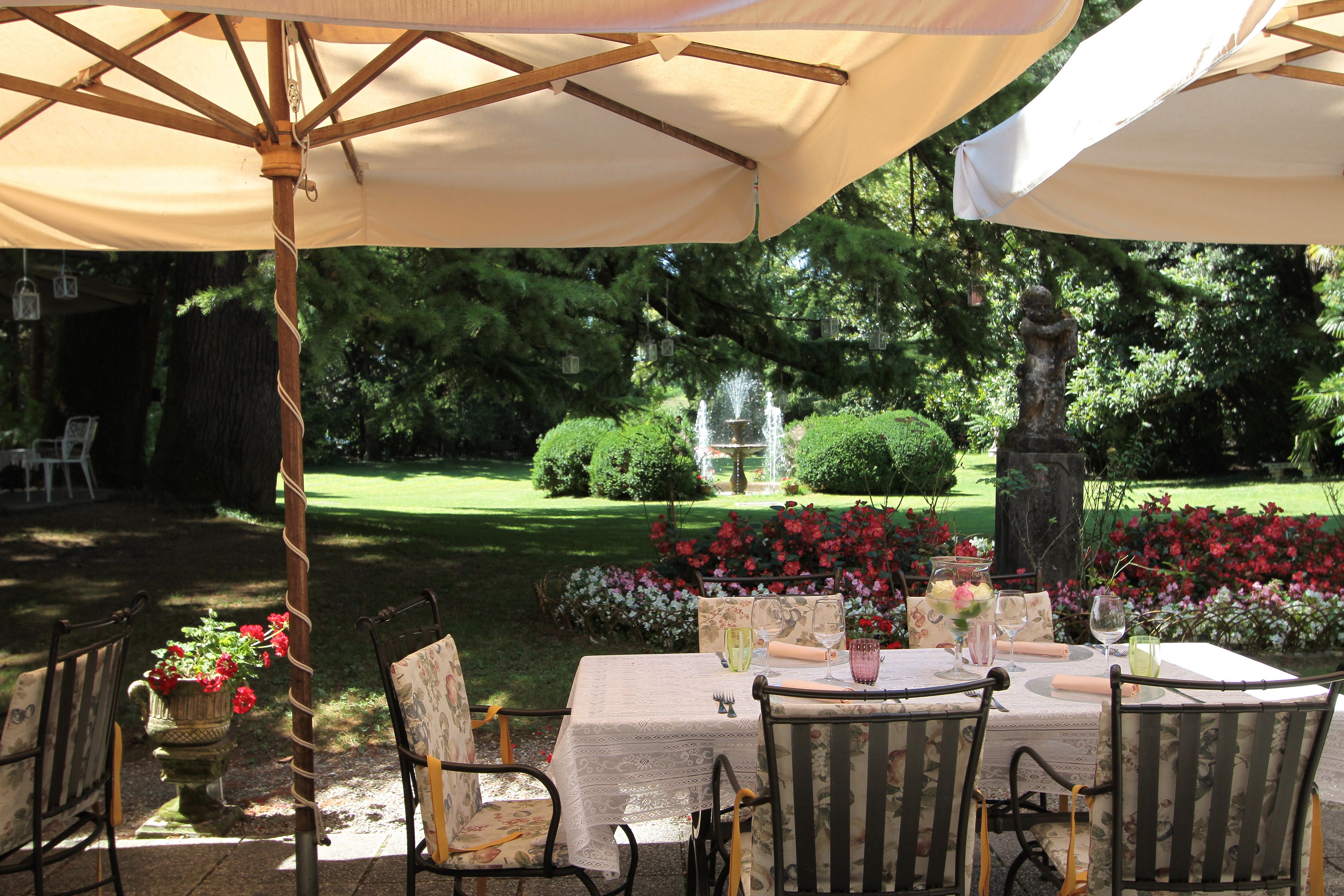 An outdoor dining area with a table set for two, surrounded by chairs, under a large umbrella.