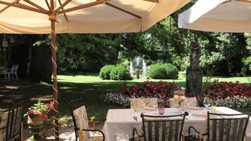 An outdoor dining area with a table set for two, surrounded by chairs, under a large umbrella.