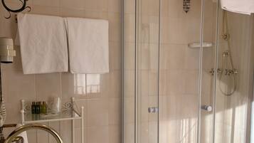 Ein Badezimmer mit einer Duschkabine aus Glas, einem Waschbecken mit goldfarbenem Wasserhahn und einem Handtuchhalter mit zwei Handtüchern.