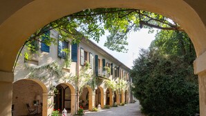 Un patio en arco con un edificio que presenta múltiples ventanas y balcones, rodeado de follaje y un sendero de grava.