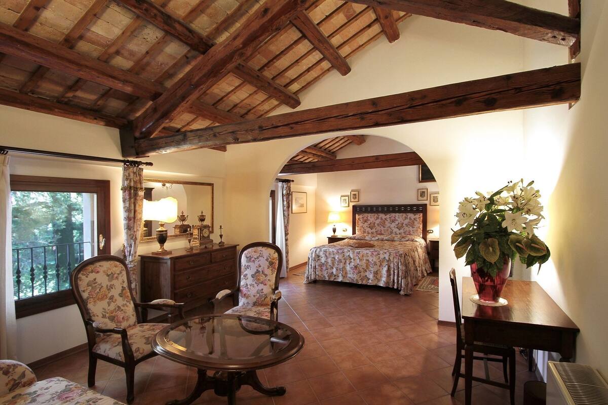 A cozy room with a wooden ceiling, a bed with floral bedding, a round table, and a chair with floral upholstery.