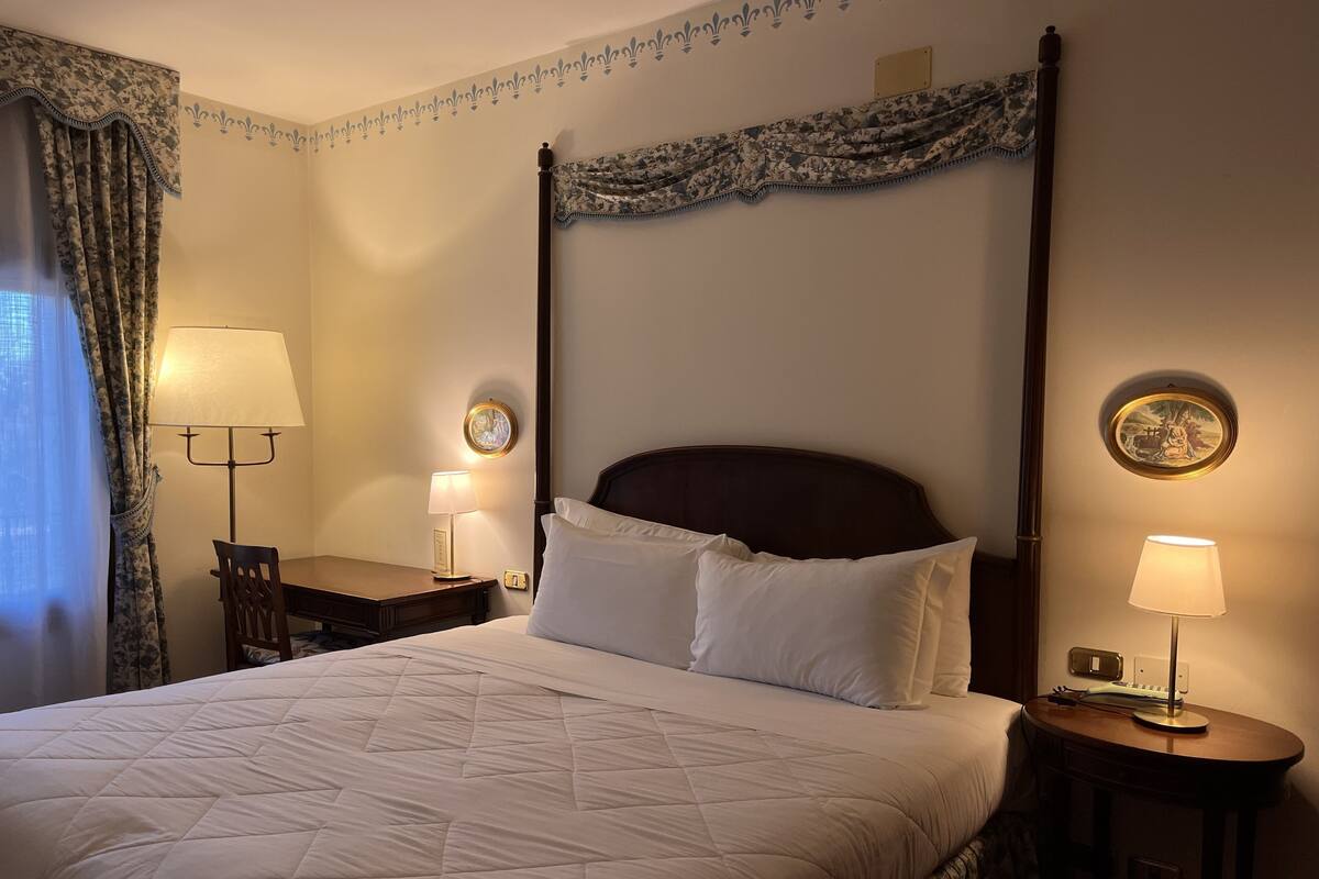 A neatly made bed with a quilted white duvet, two bedside tables with lamps, and a headboard with a floral pattern.