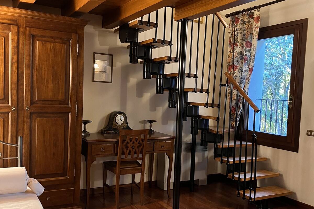 A room with a wooden staircase, a desk, a chair, and a bed.