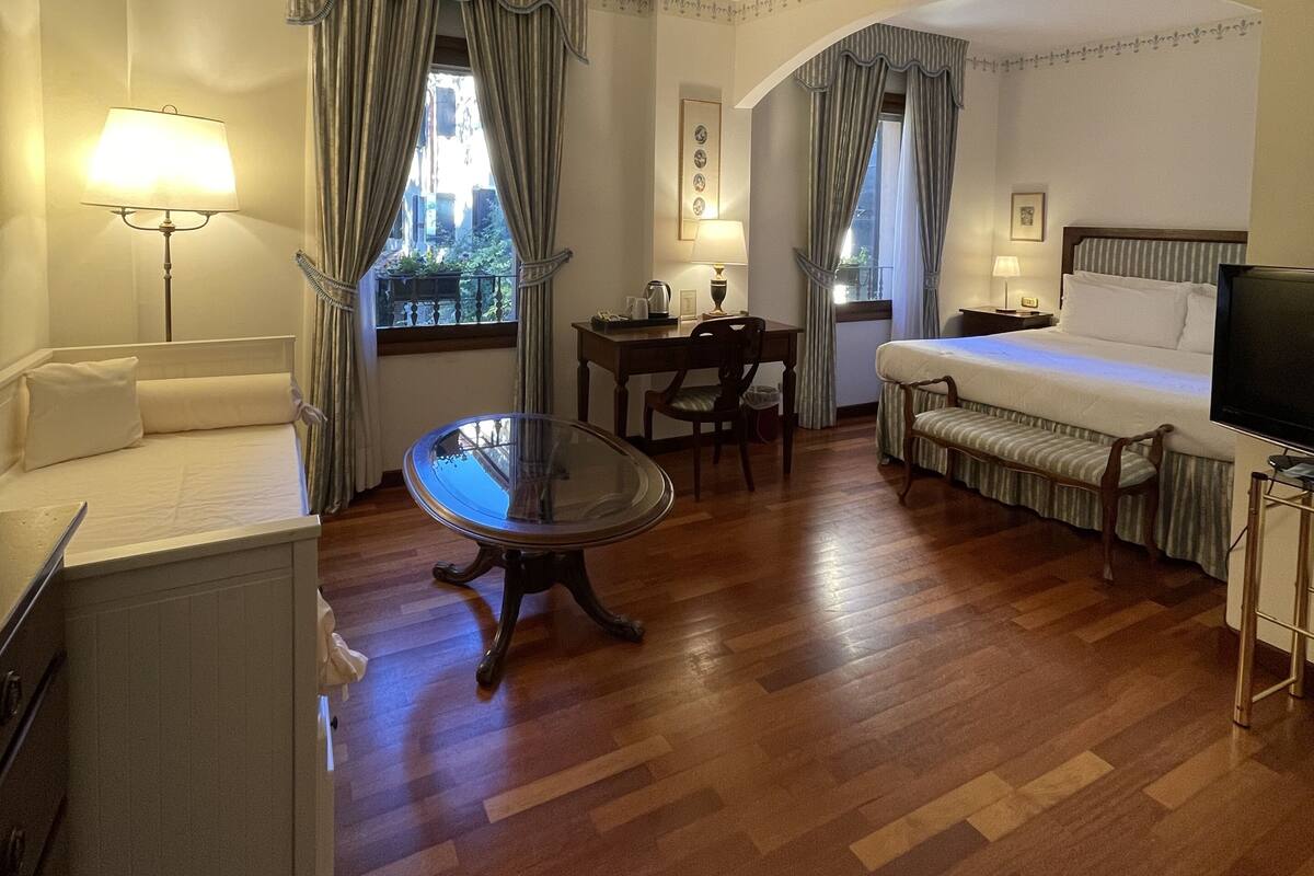 A hotel room with a bed, a desk, a chair, a table, and a TV.