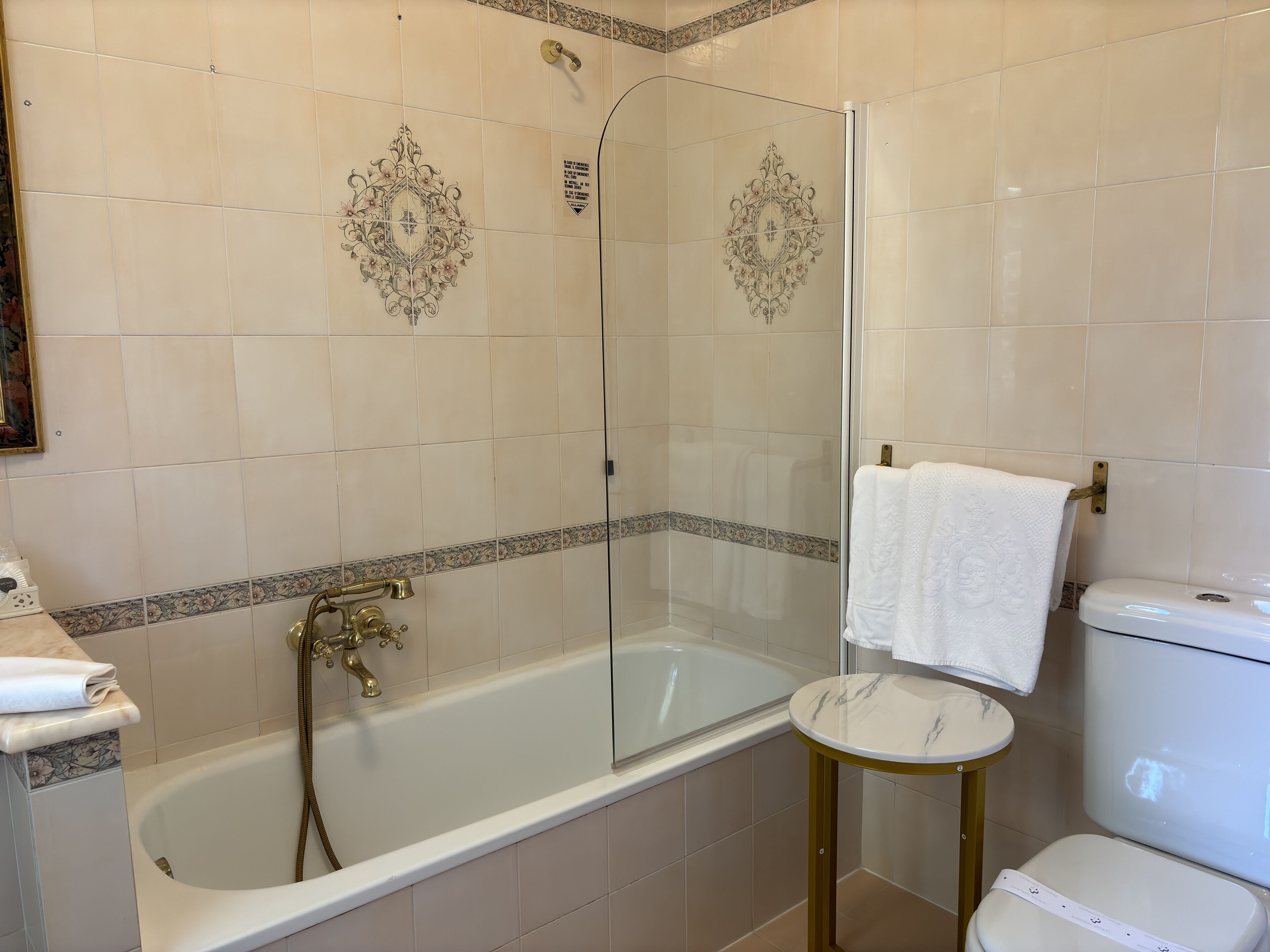Bagno con vasca, cabina doccia in vetro, servizi igienici e un piccolo tavolo rotondo con un asciugamano.