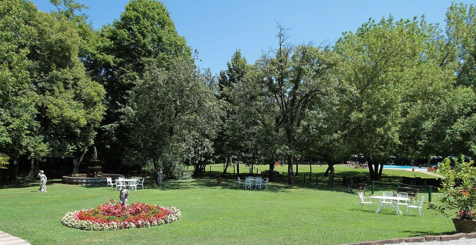 A well-maintained lawn with a circular flower bed, several white plastic chairs, and a statue in the foreground.
