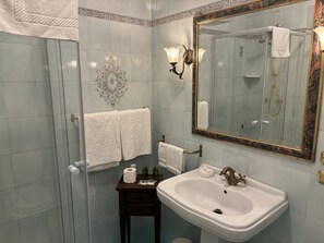 Ein Badezimmer mit Duschkabine aus Glas, einem weißen Waschbecken mit goldfarbener Armatur und einem dekorativen Spiegel mit Blumenrahmen.