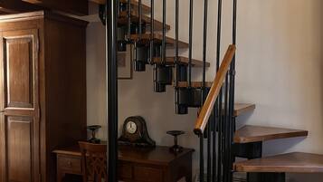 Una escalera de madera con barandillas de metal negro, una mesa de comedor con sillas y un reloj fijado a la pared.