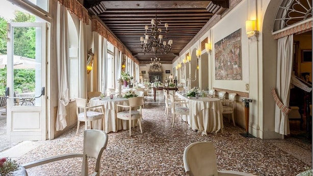 Un restaurante con varias mesas y sillas, un candelabro y grandes ventanales.
