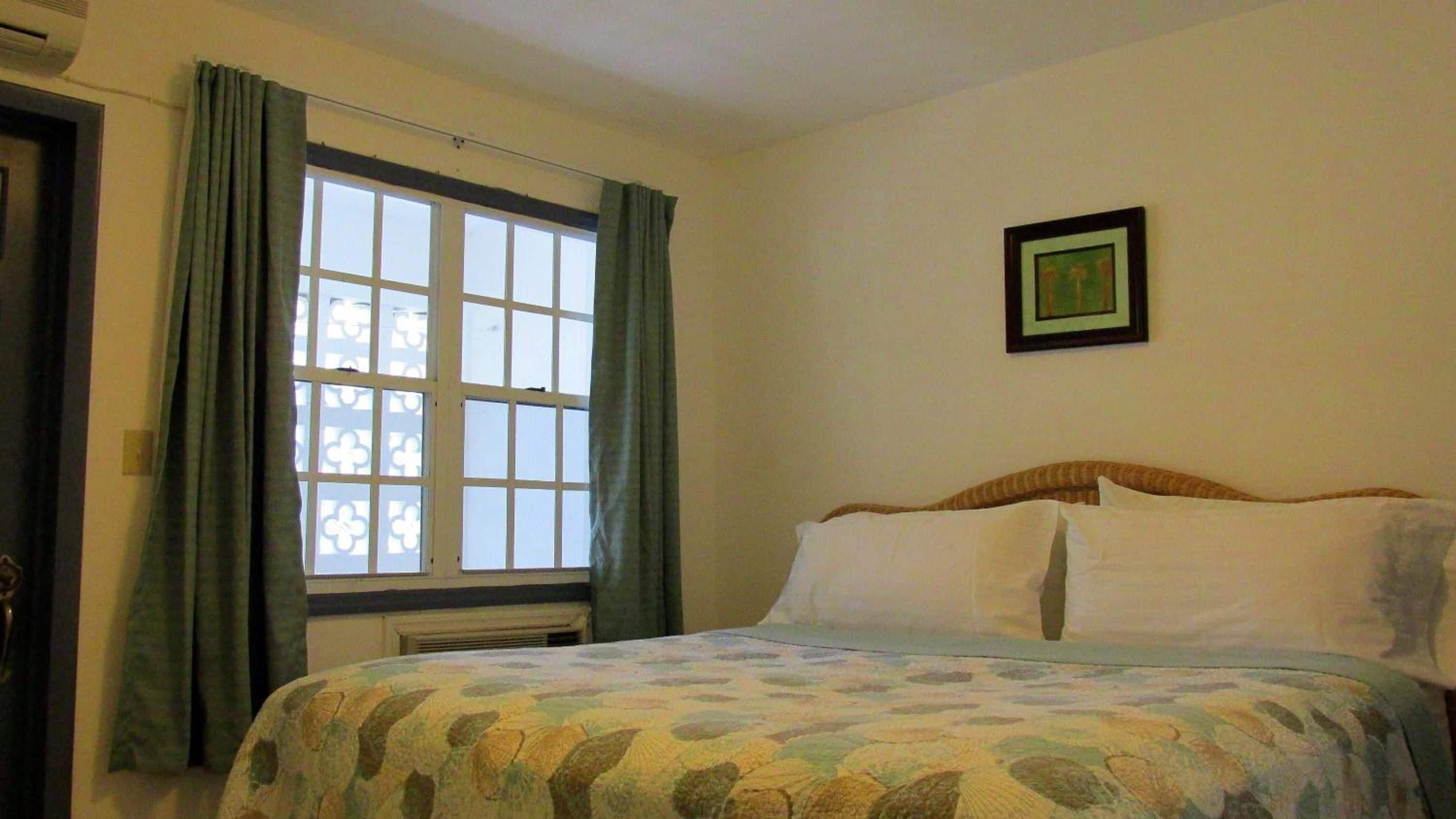 A bedroom with a bed, a window with curtains, a radiator, and a framed picture on the wall.