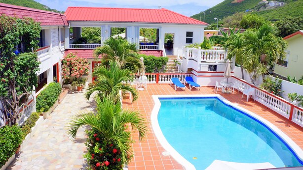 Una piscina con techo rojo, rodeada de plantas en macetas y una valla blanca.