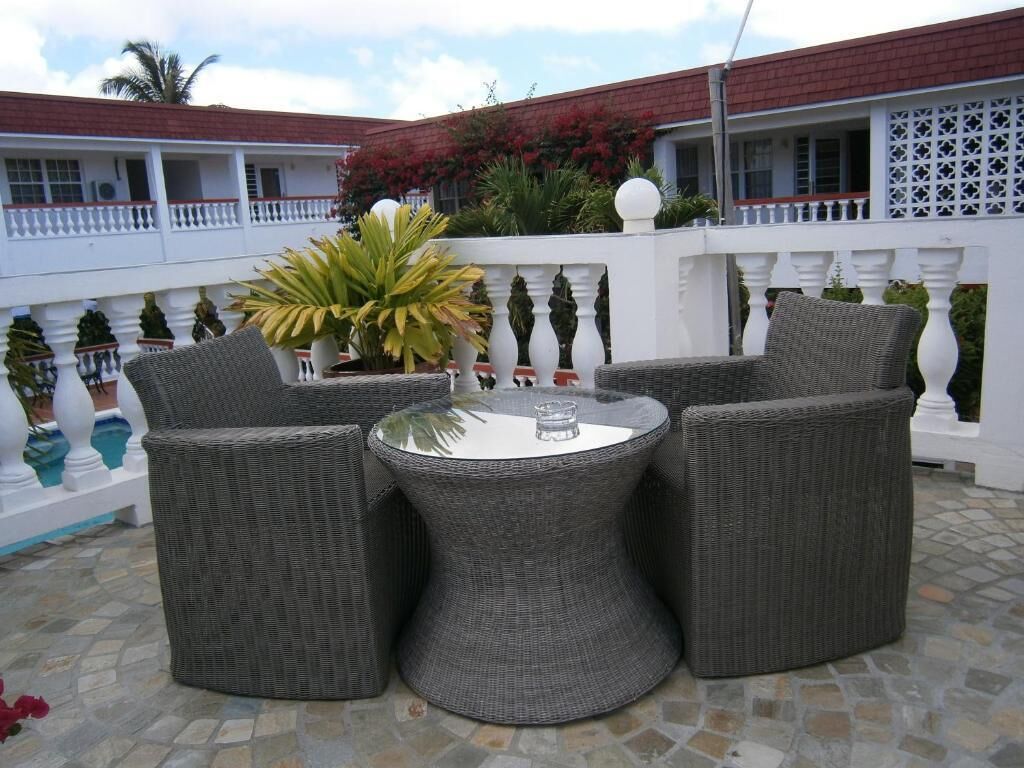 Un patio con mobiliario de mimbre, una mesa redonda y una barandilla blanca.