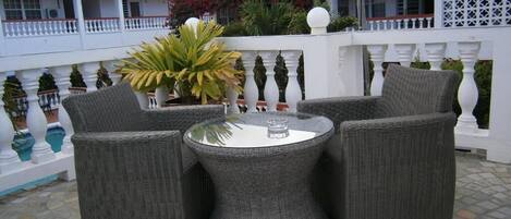 Un patio con mobiliario de mimbre, una mesa redonda y una barandilla blanca.