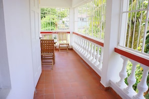 A covered balcony with tiled flooring, wooden chairs, and white balustrades. - L'Esperance Hotel (Philipsburg)