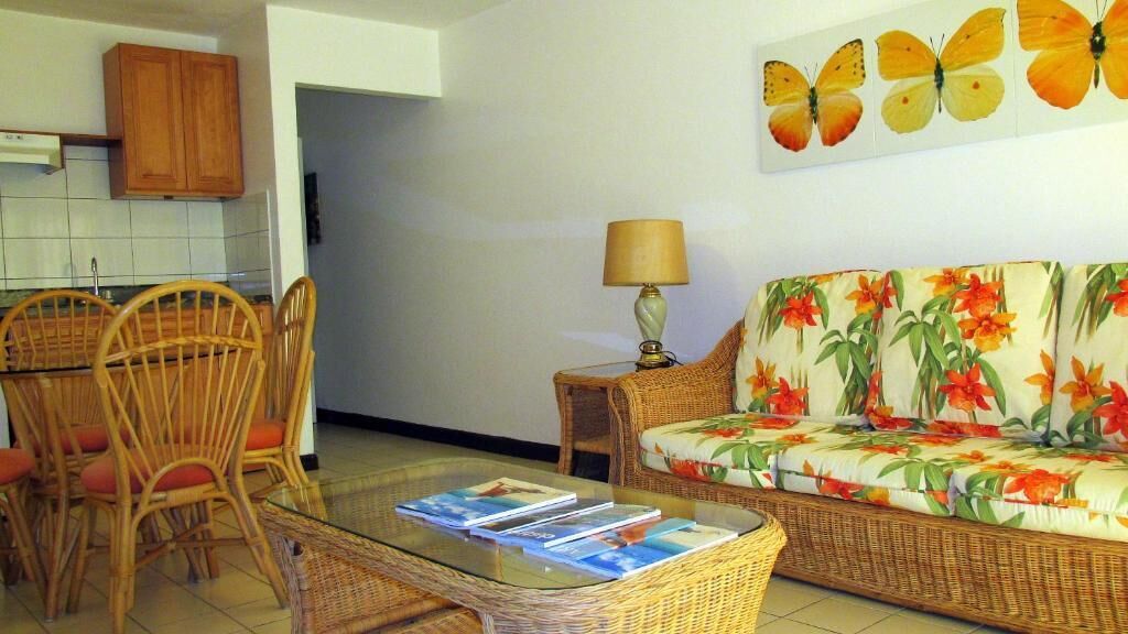 A living room with a sofa, a glass coffee table, and a dining area with wicker chairs.