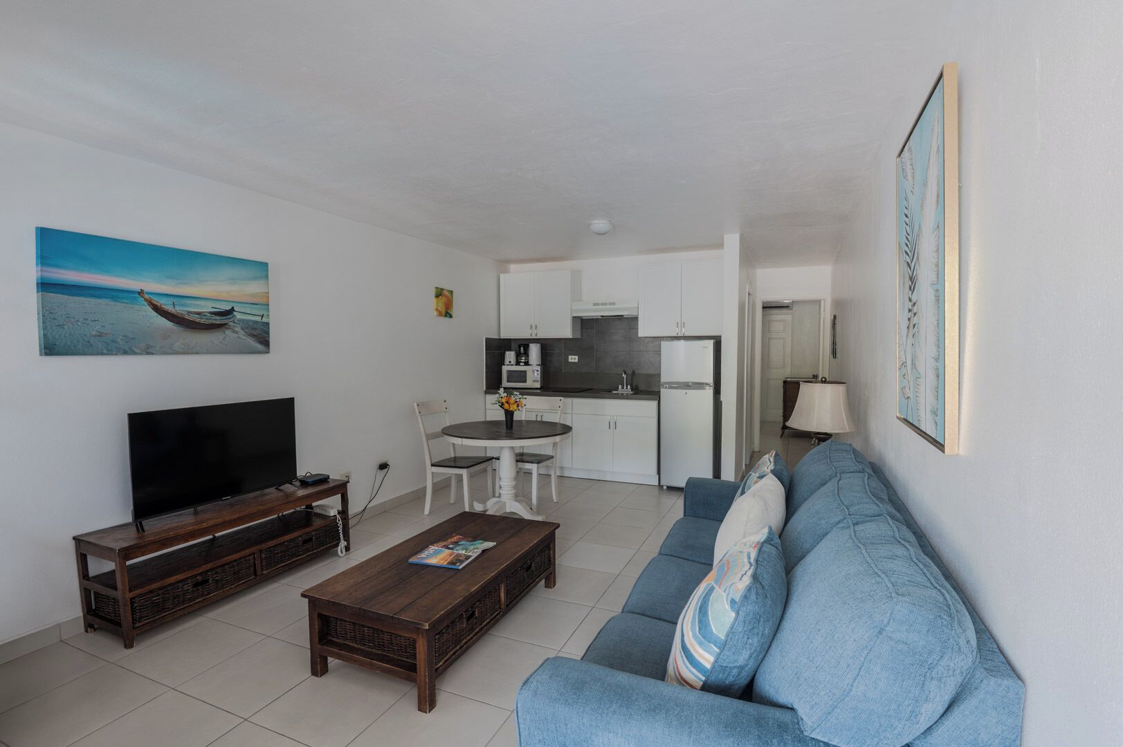 Una sala de estar con televisor, mesa de centro, sofá y un cuadro de un barco en la playa.
