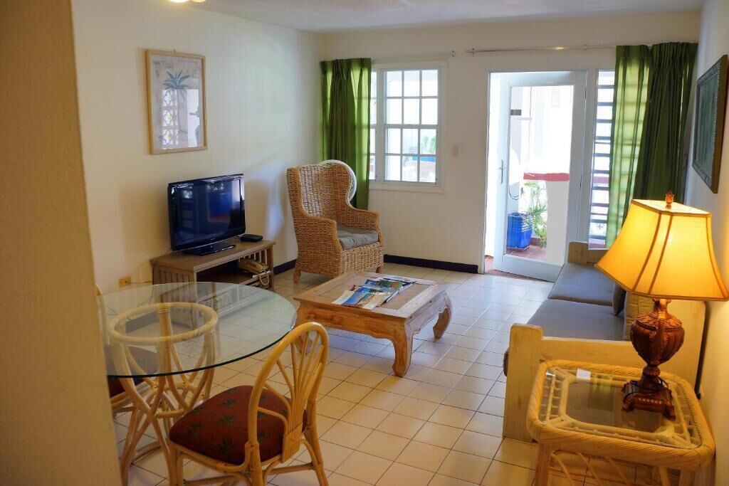 Una sala de estar con una mesa de vidrio, sillas de mimbre, un sofá, un televisor y una lámpara.