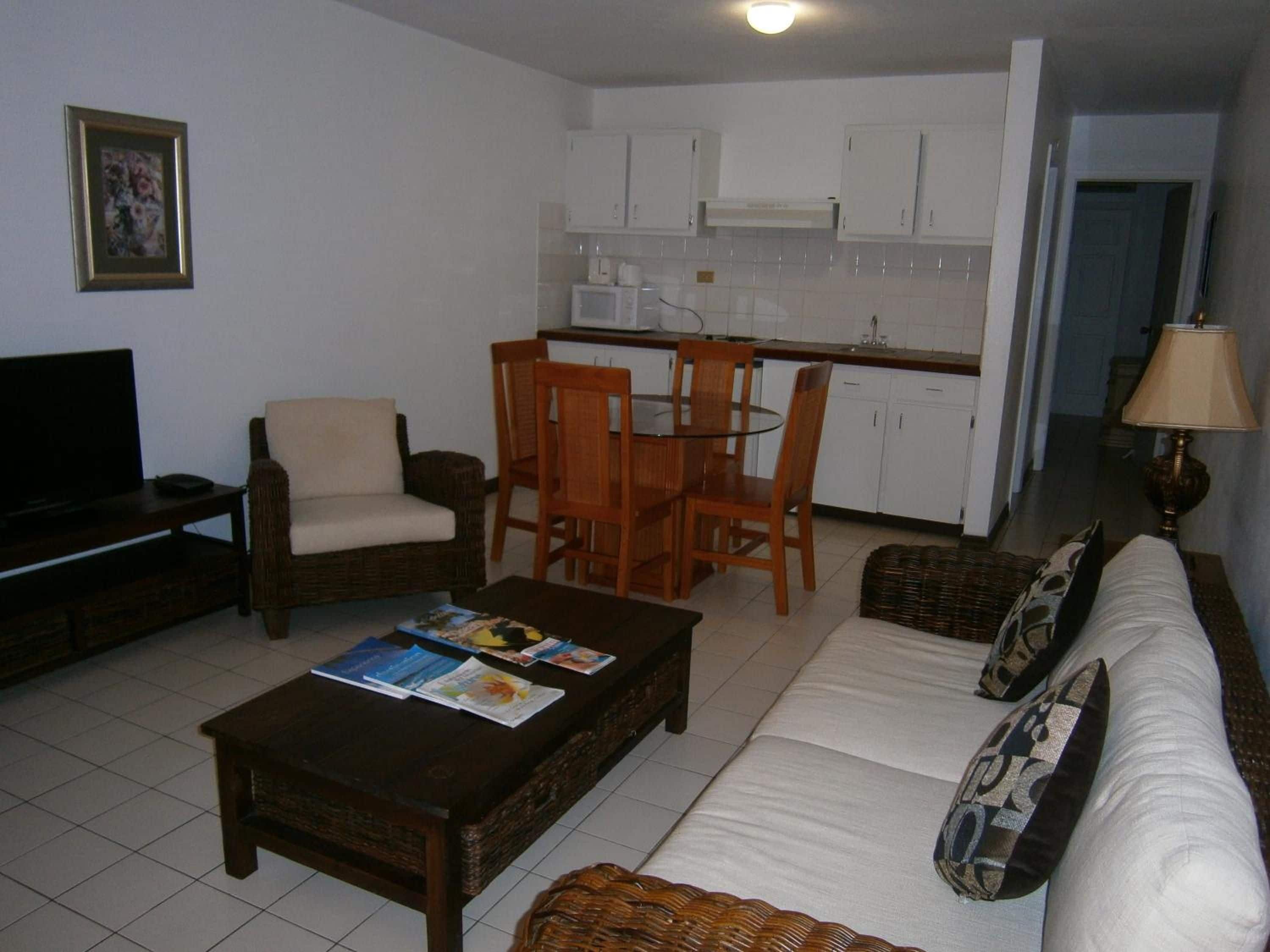 A living room with a sofa, a coffee table with magazines, a television, and a dining area with chairs and a table.