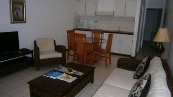 A living room with a sofa, a coffee table with magazines, a television, and a dining area with chairs and a table.