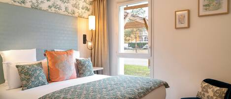 A hotel room with a bed, a chair, a window, and a wall with artwork.