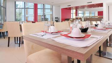 Un espace repas moderne, avec des tables et des chaises disposées de manière ordonnée, et une vue sur la cuisine en arrière-plan.